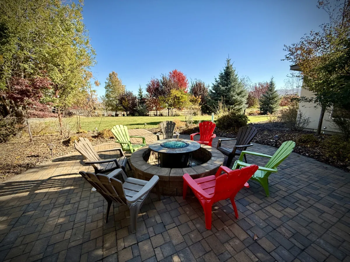 A cozy fire pit area with colorful chairs arranged in a circle, surrounded by abundant foliage. The space invites guests to gather for conversation, relaxation, and stargazing, evoking memorable evenings spent by the fire.