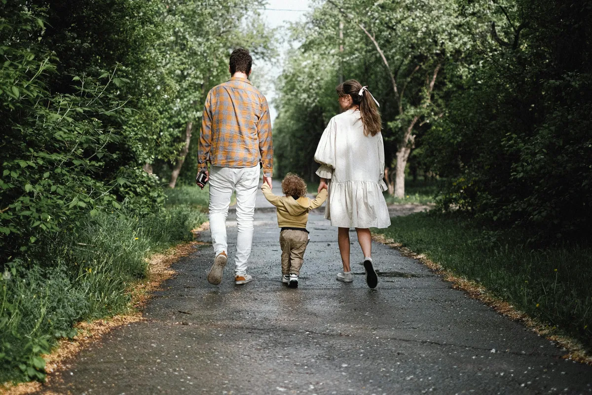 A family walks hand-in-hand along a scenic outdoor path surrounded by lush greenery, capturing a joyful moment of togetherness in nature.