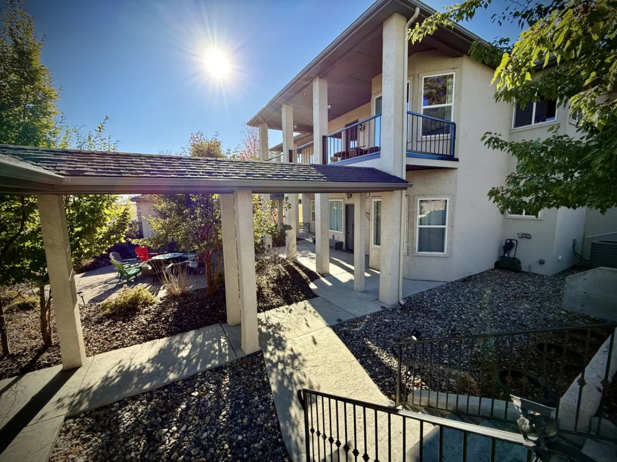 This image showcases a sunlit porch furnished with green chairs, porch columns, and vibrant flowering plants. The setting is bright and inviting, suggesting a perfect spot for outdoor dining, relaxing, or social gatherings. Sunset light bathes the area, reinforcing the connection to scenic views and tranquil outdoor moments.