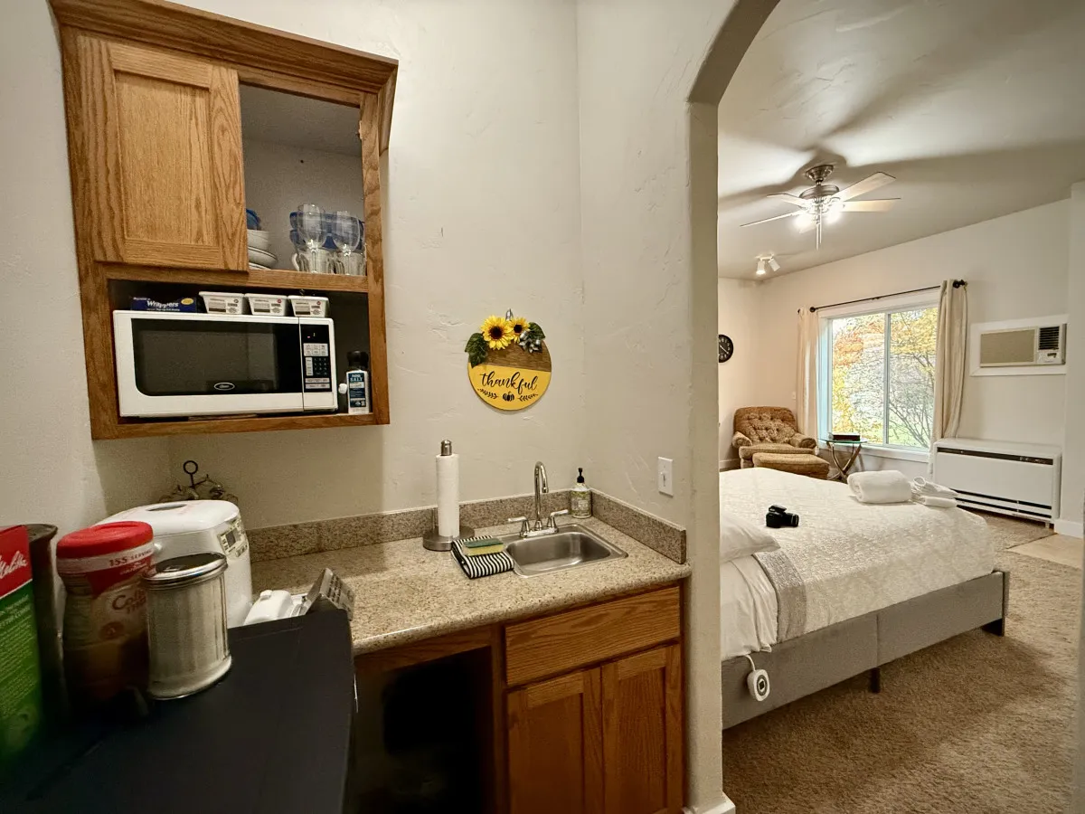 A studio suite with a compact kitchenette, decorative sign, and comfortable bedroom area. Practical appliances and soft lighting make the space feel both functional and welcoming, representing the casita amenities.