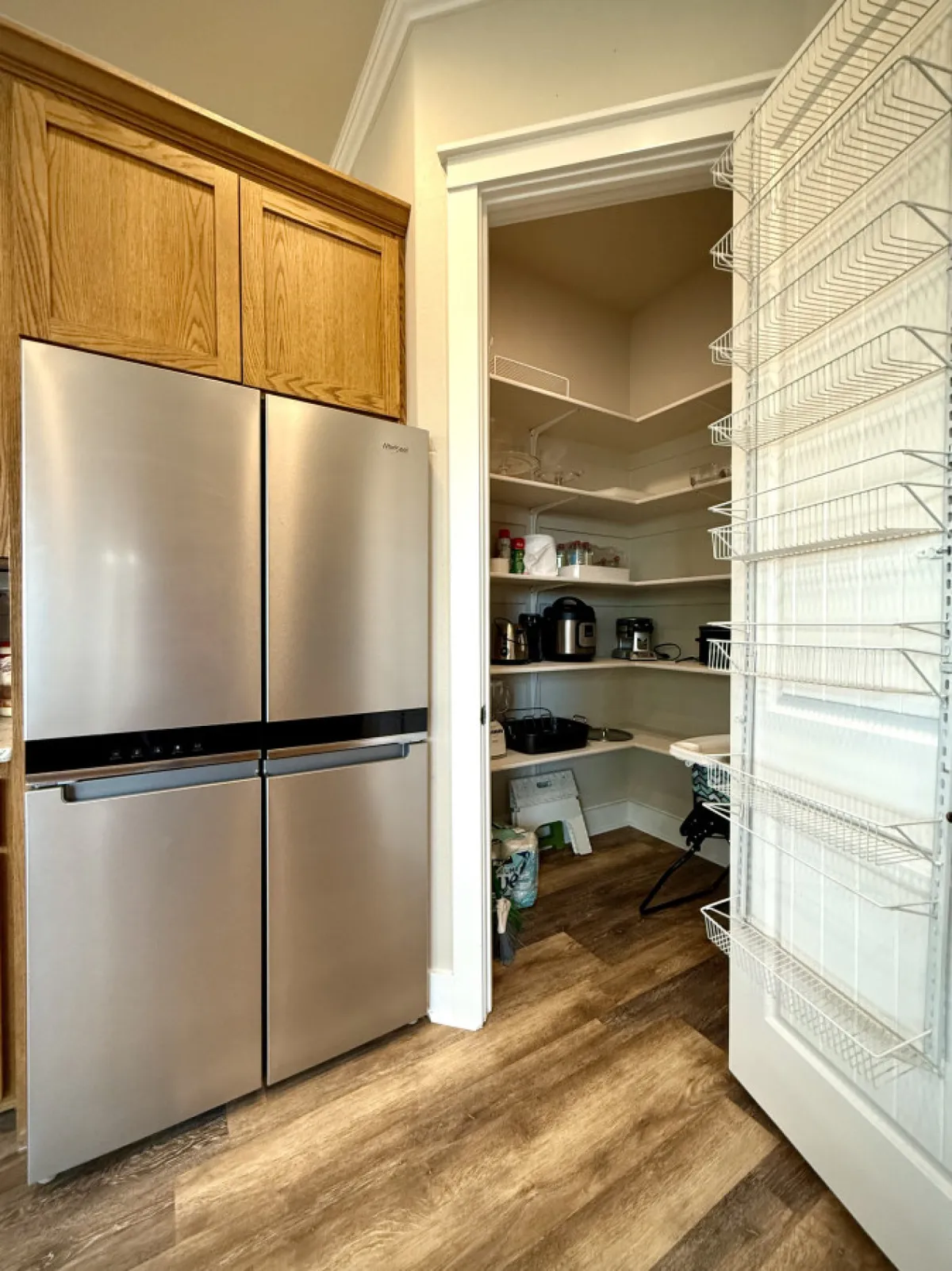 A well-organized kitchen area featuring a stainless steel refrigerator, open pantry door, and tidy pantry shelves. The scene suggests easy access to ingredients and a practical layout for meal prep and group cooking.