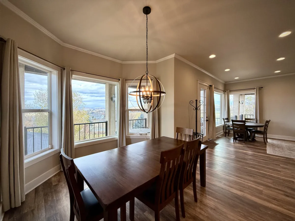 A formal dining table sits beneath a chandelier, surrounded by large windows that frame breathtaking views. The warm and welcoming atmosphere is ideal for family meals, celebrations, and entertaining guests.