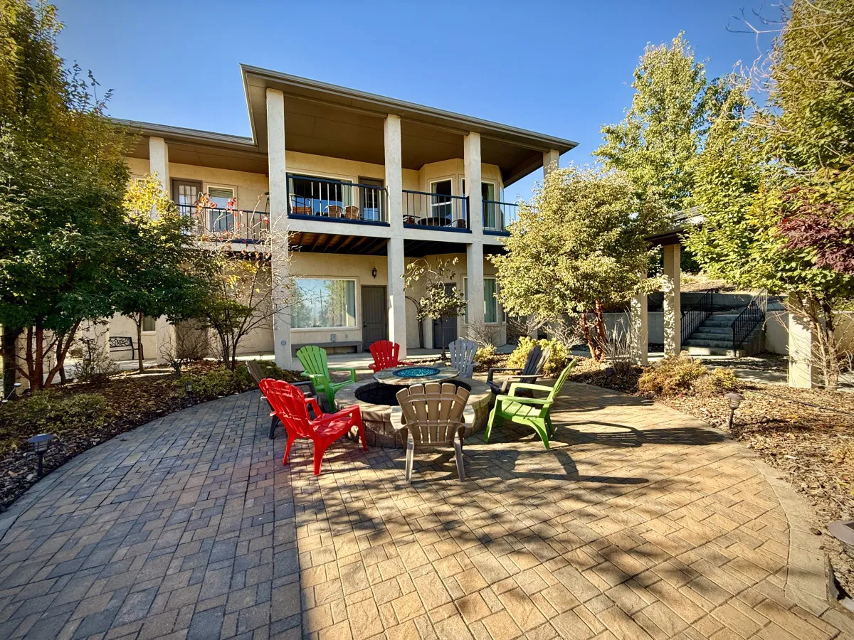 A welcoming backyard scene with a fire pit encircled by colorful chairs, lush landscaping, and balconies overlooking the outdoor space, suggesting a place for social gatherings and relaxation after a day of adventure.